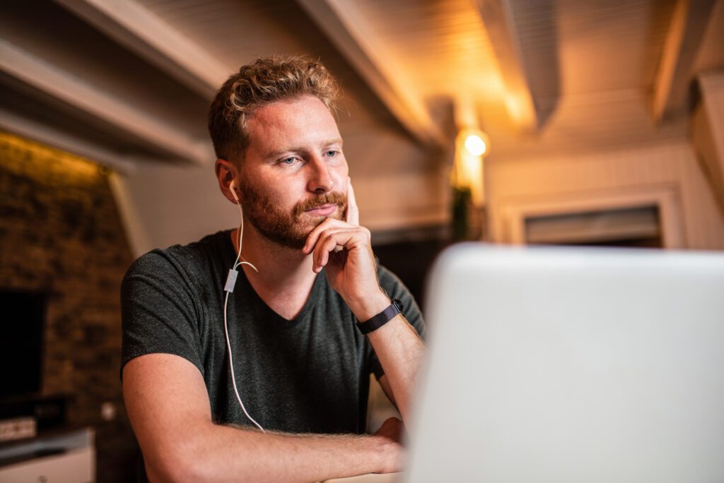 A man wears earphones while looking at something on his laptop