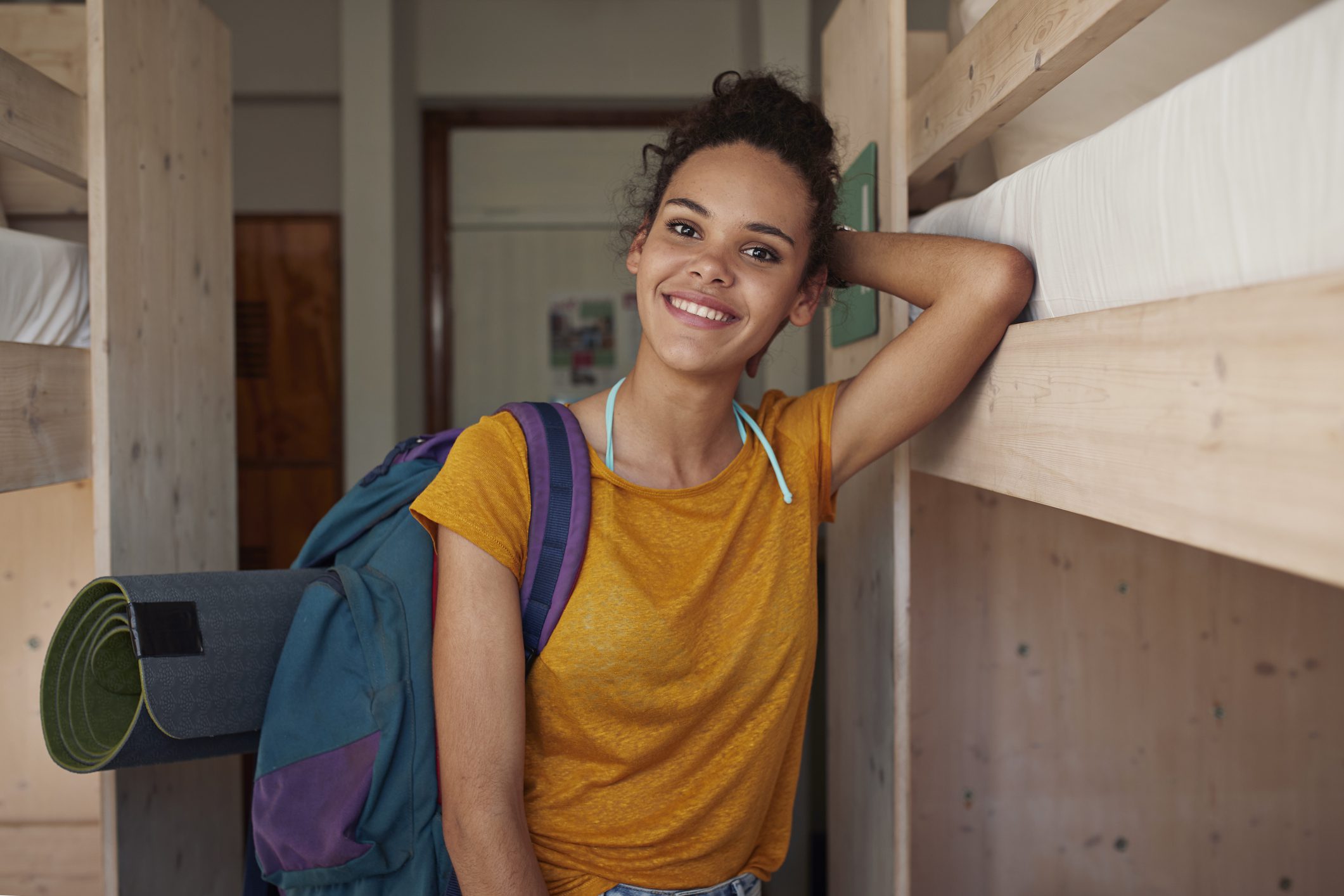 A teenage girl holds a backpack over her shoulder as she smiles