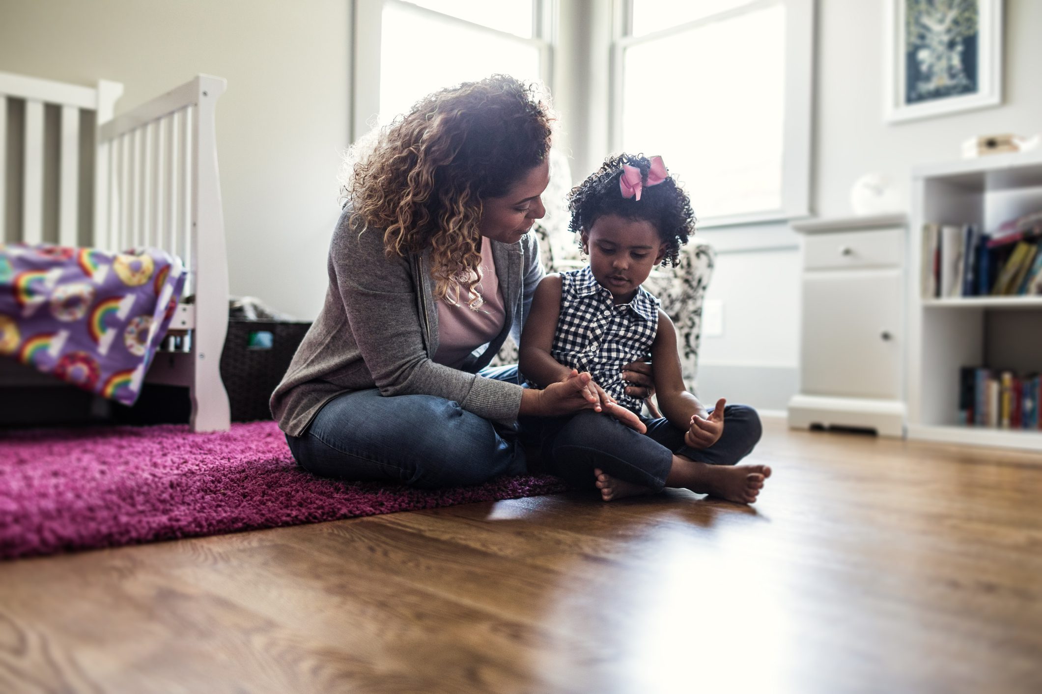 A mother sits on the floor with her child as she speaks to her