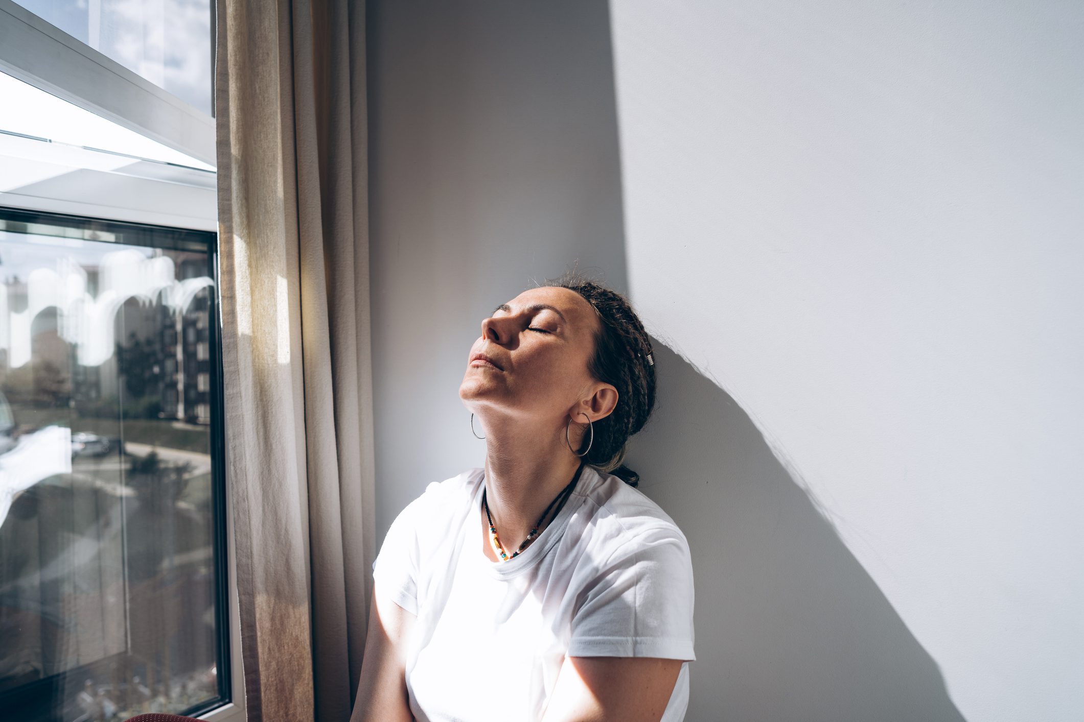 A depressed woman leans on a wall while looking out a wind