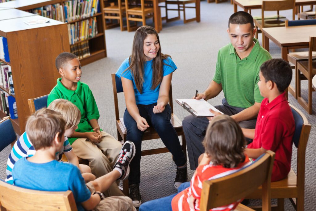 A group of children and a therapist sit in a circle for group therapy