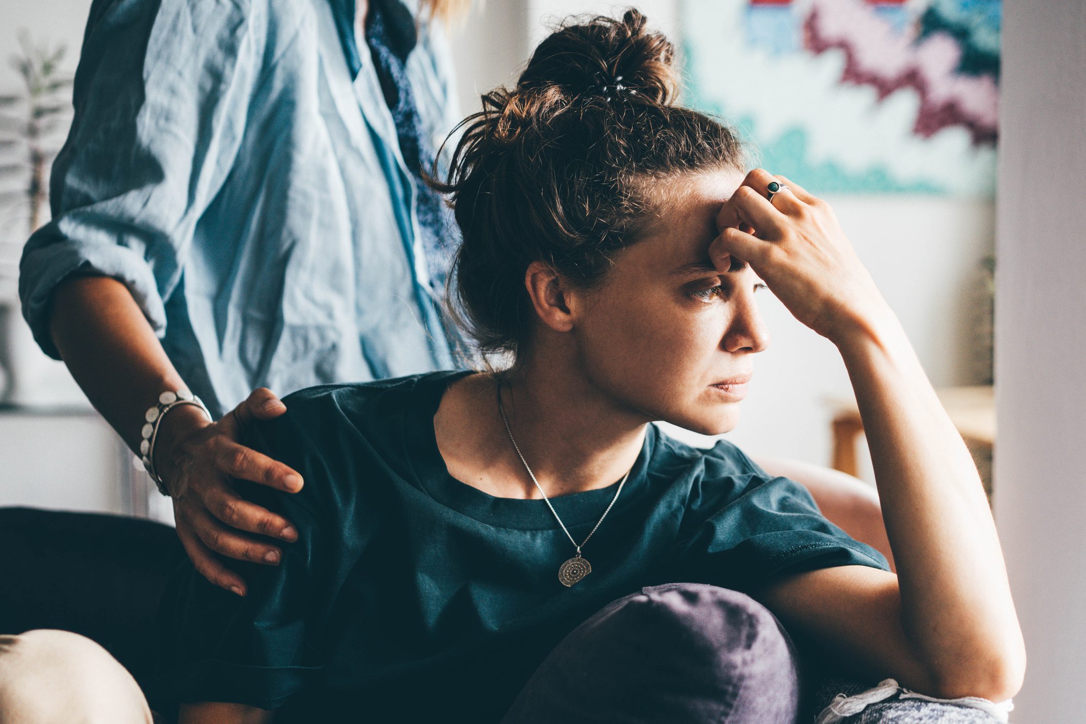 Distressed woman holds a hand to her forehead while a man behind her comforts her.