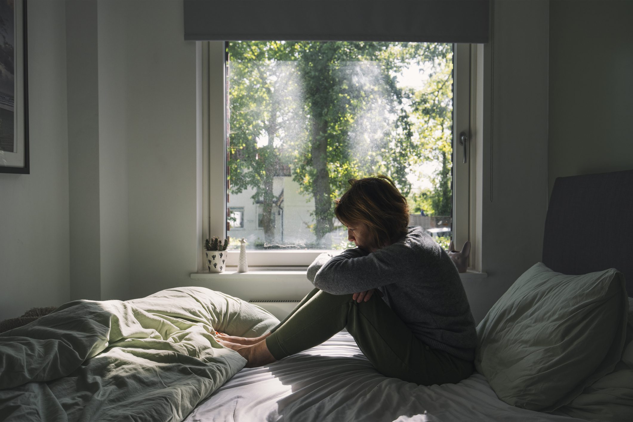Depressed teen sits alone on their bed in a dark room.