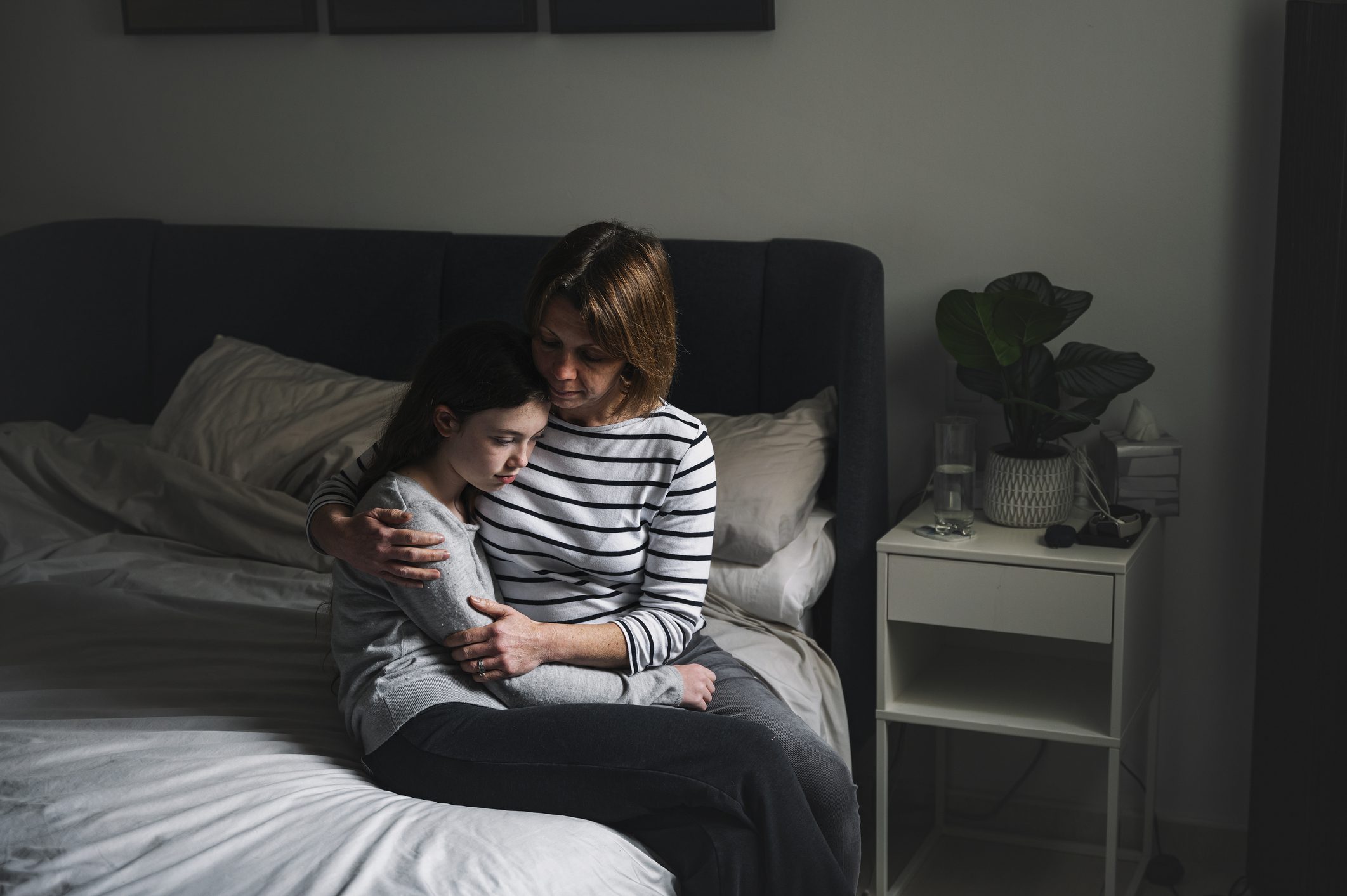 A mother comforts her traumatized child as they sit at the edge of her bed.